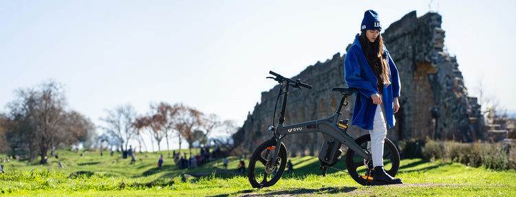 A woman wearing a blue hat is riding a DYU T1 electric bicycle in winter. The ebike features a magnesium alloy frame and a torque sensor for a smooth and efficient ride.